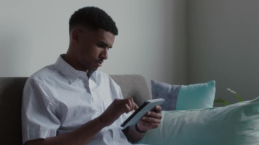 A man is sitting on a couch using an tablet computer