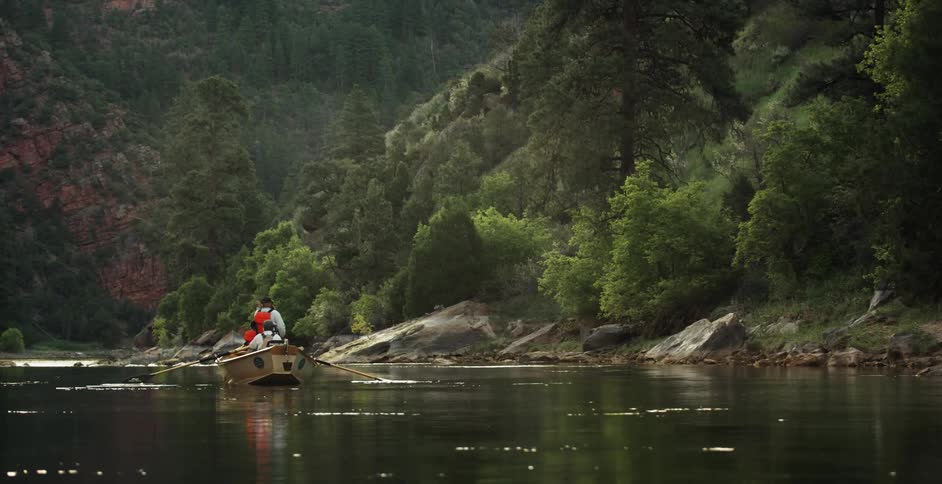 Two people paddle a boat down a stream