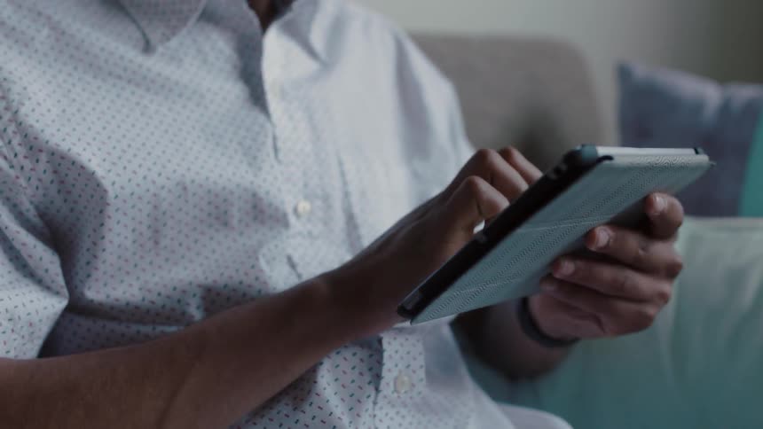 A man is sitting on a couch working on a tablet device