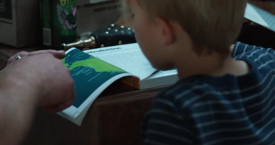 Child looks at a book with an adult pointing at the pages