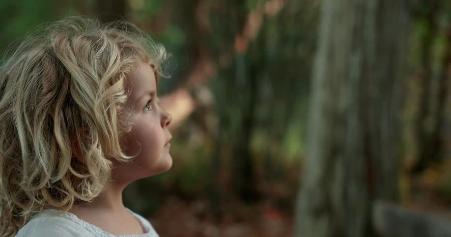 A young girl stands outside under a tree
