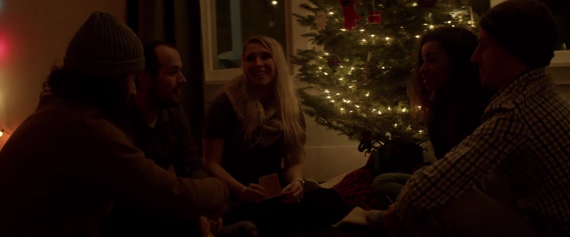 A group of friends sit on the floor talking and playing cards