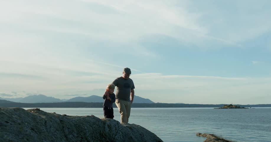 Man and child walk on rocks near a lake