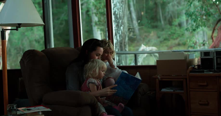 Man woman and child sit in a chair next to a large window reading a book