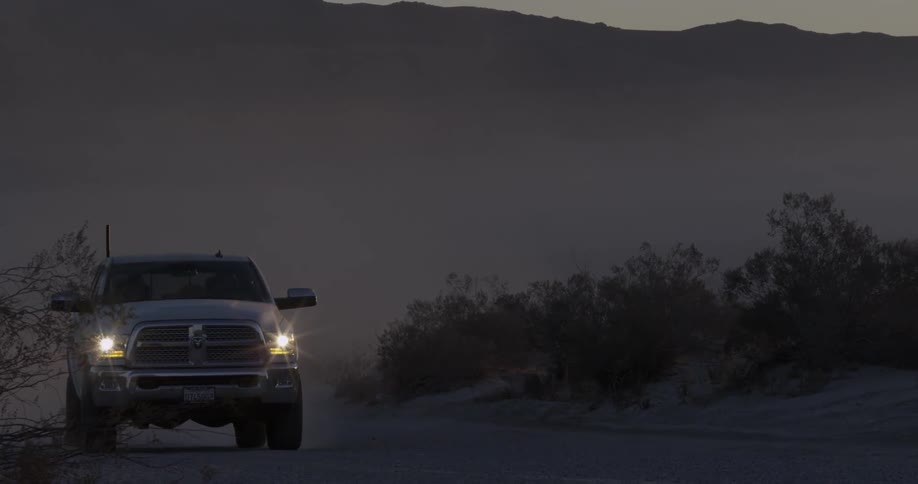 A truck drives on a dirt road at sunset