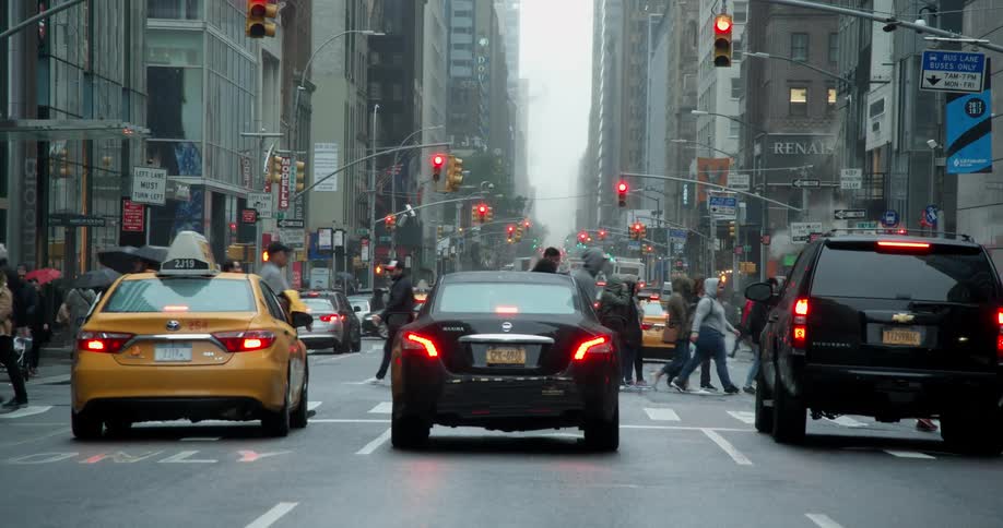Pedestrians cross a busy city street on a rainy day
