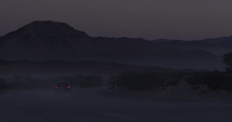 A truck's rear lights are visible as it drives on a dirt road