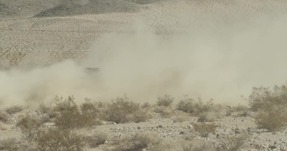 An off road vehicle drives and spins in a desert while kicking up dust