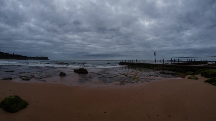 Dark clouds hover over a beach and boardwalk area