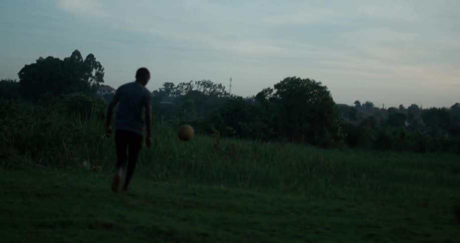 Boys play soccer in a field at sunset