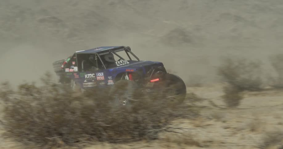 An off road vehicle drives through a desert and kicks up dust