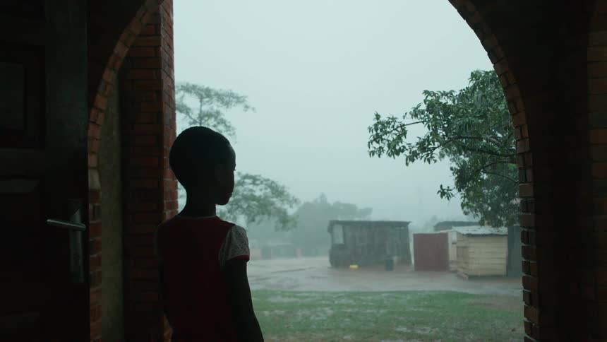 A boy watches a rainstorm while standing next to a building