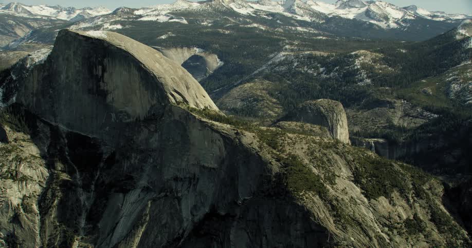 A rocky mountain range is dotted with snow on a clear day near Half Dome in Yosemite National Park, California