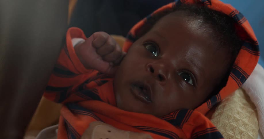 A person adjusts the clothes on an infant boy
