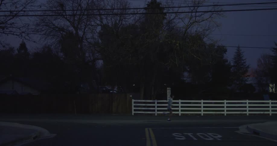 A man jogs down an empty street in front of some fences at dusk