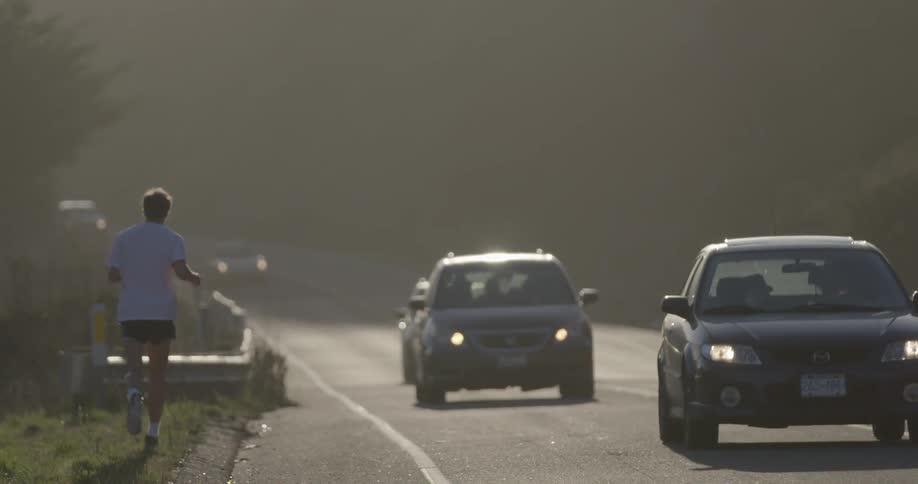 A man jogs down a street as cars pass by in the day time