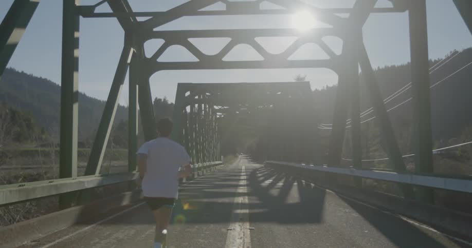 Man jogs on a bright sunny morning on a narrow bridge