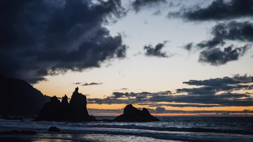 Clouds move across a beach as the sun sets