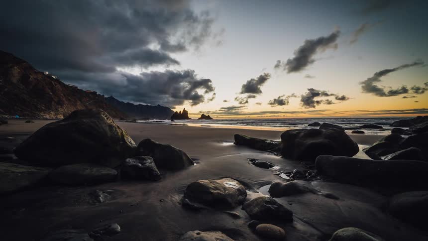 Clouds billow and roll over a rocky beach at sunset