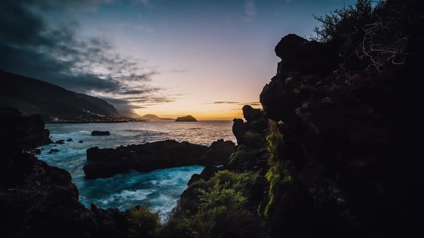 The sun is setting beyond a city on a rocky coastline