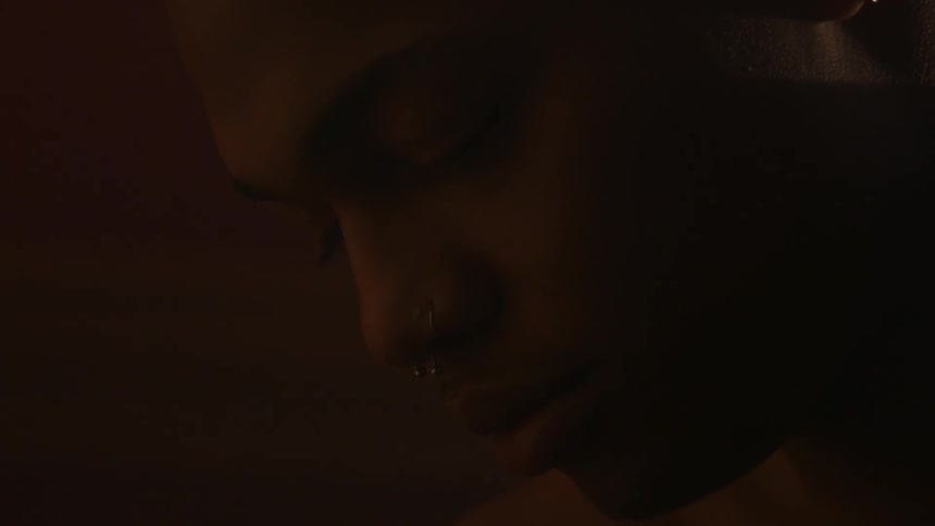 A man with nose piercings sits with his head bowed