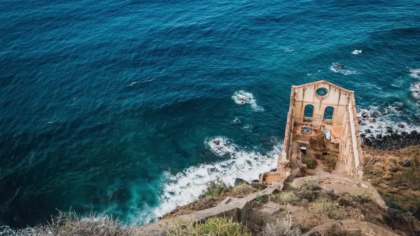 Waves are crashing along the shore next to the ruins of an old church