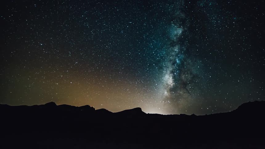 The milky way and stars are moving in the night sky over a desert landscape