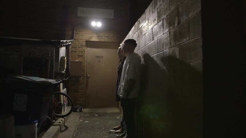 Three people stand with their backs against a brick wall