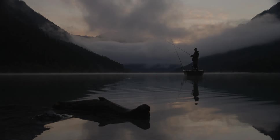 Lone man stands fishing in a small boat under a cloudy sky