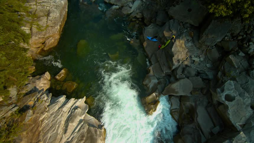 Kayakers portage their kayaks past rapids in a rocky gorge