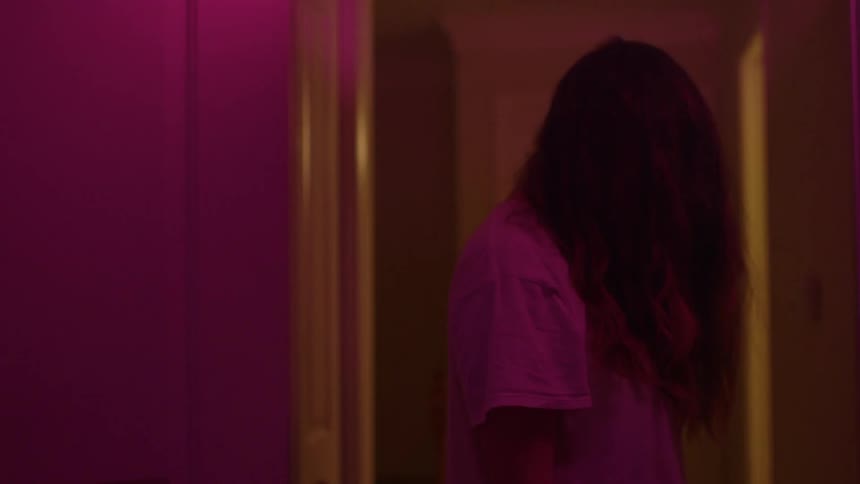 A woman stands in a purple illuminated hallway