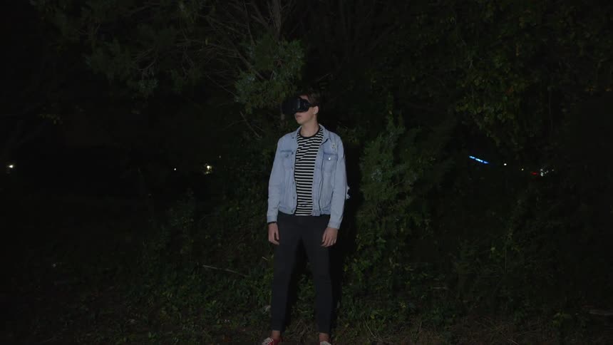 A man wearing vr glasses stands outside in the evening