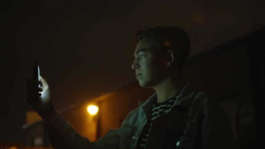 Young man looks at his bright cell phone screen