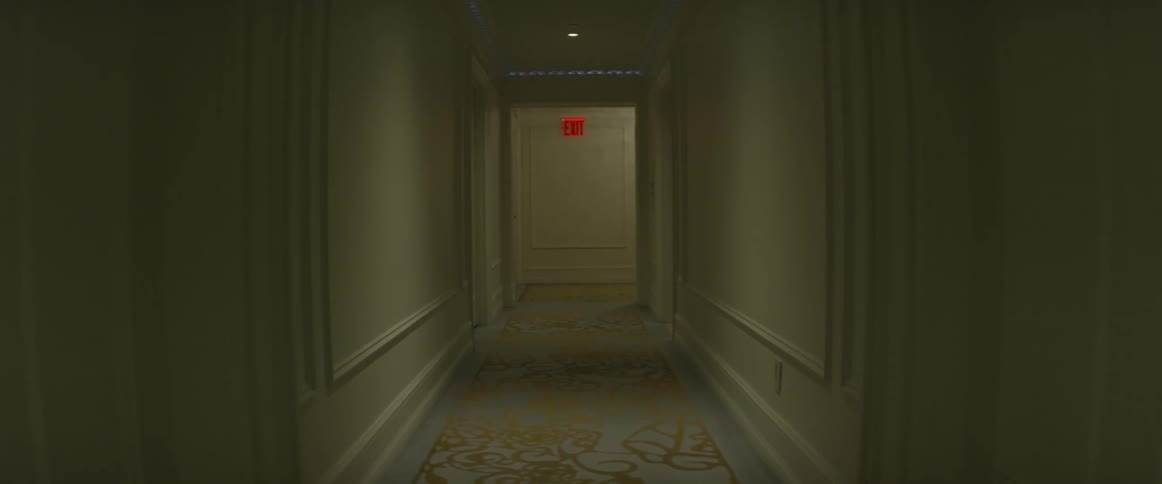 An exit sign glows at the end of a hotel hallway