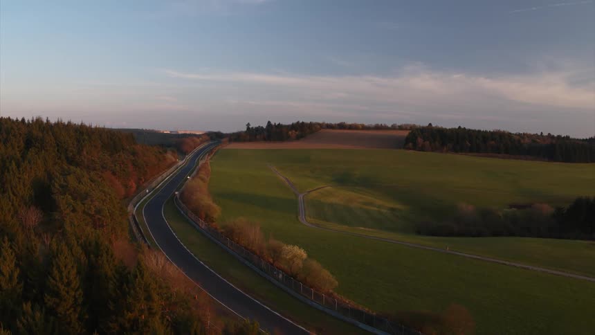 An empty roadway sits between a field and trees