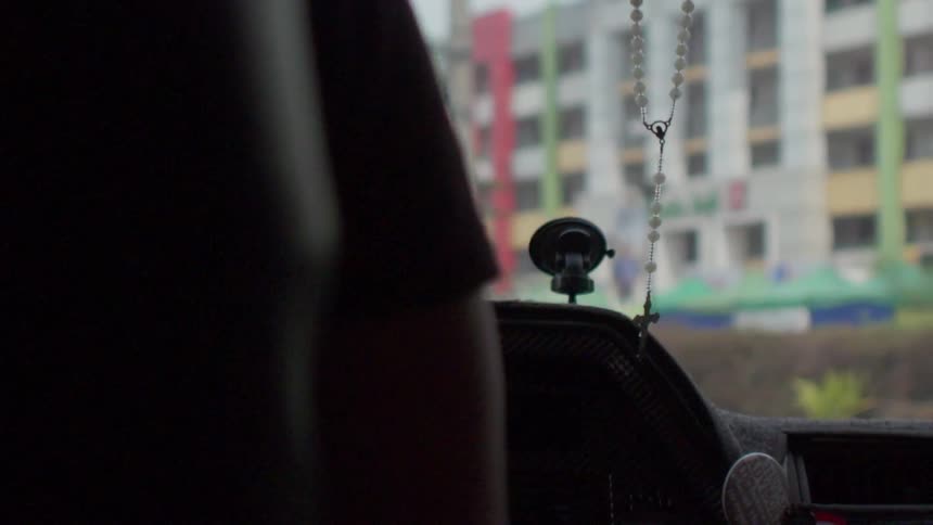 A person drives with a rosary on their rearview mirror