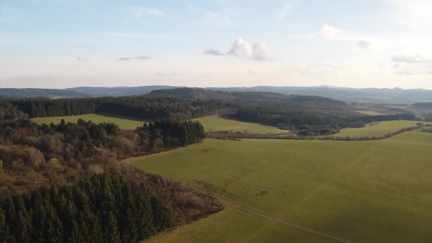 Green farm fields stretch out between forests during the day
