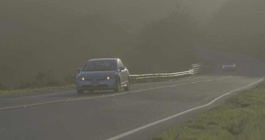 A person jogs down a foggy road as cars pass by