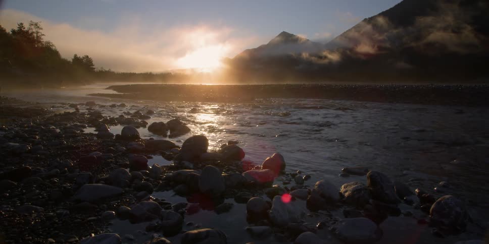 Water laps a lakeshore in a mountain landscape at dusk