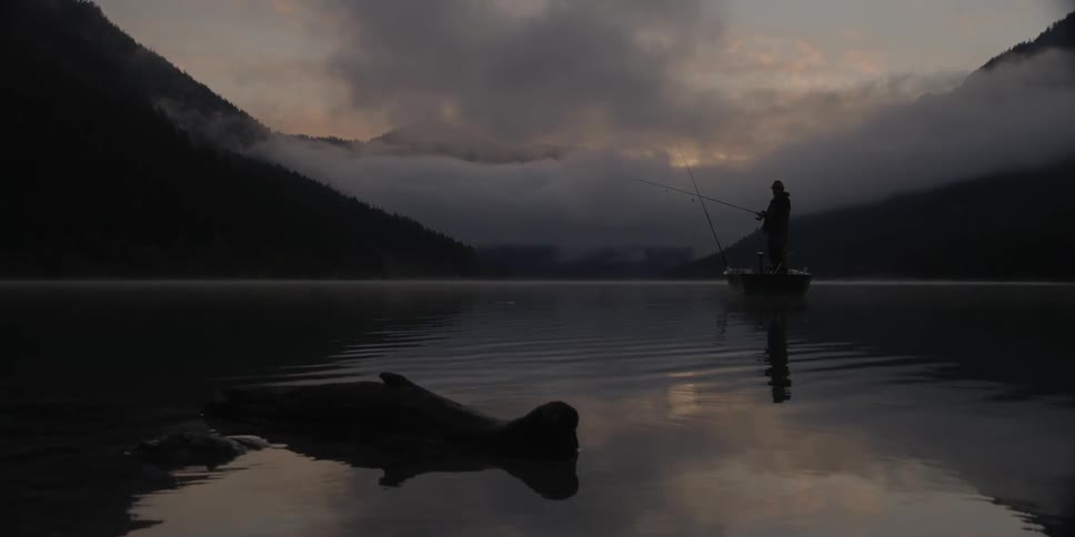 A man stands in a boat fishing at dusk or dawn