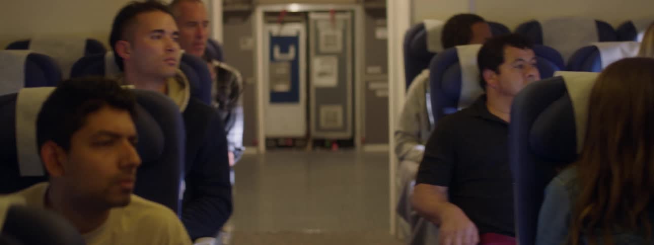 A group of passengers on an airplane are looking concerned