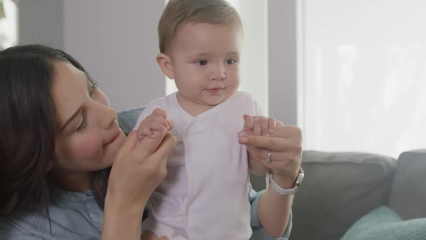 A woman sitting on a couch is playing with a baby