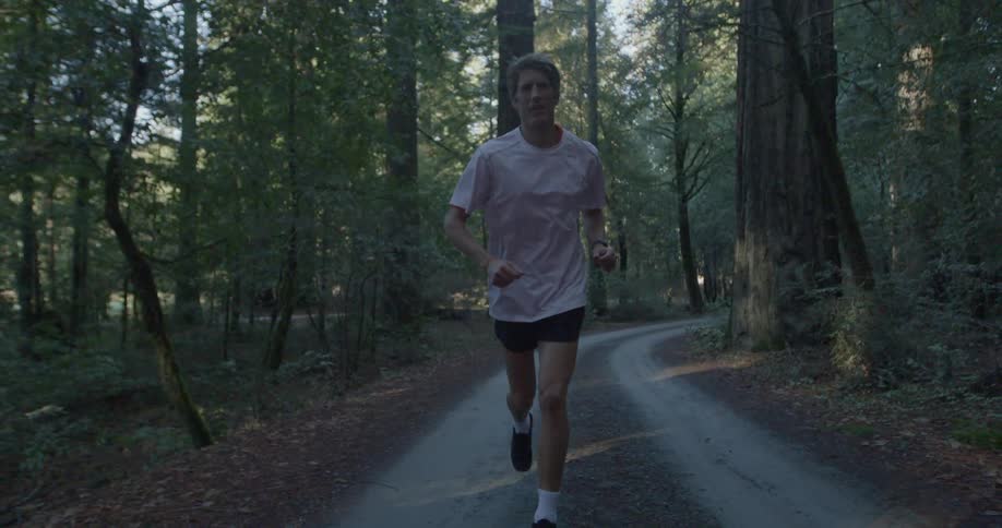 Male runs along a dirt road in a heavily wooded area where both sides of the road are covered with dried leaves