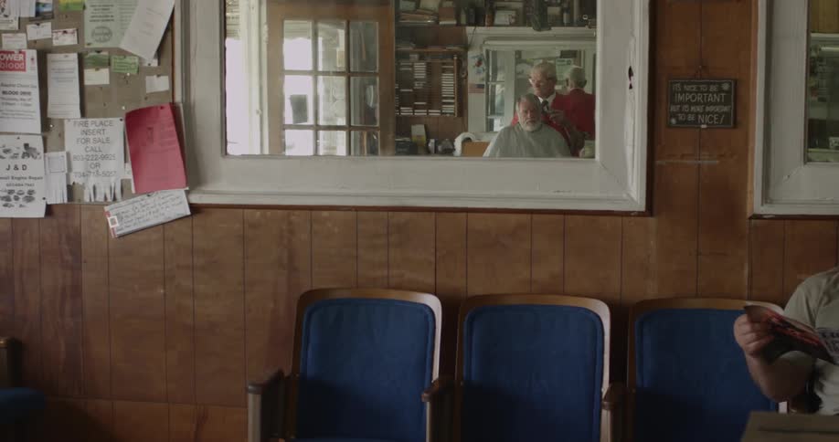 Blue chairs in a barbershop with a patron getting a haircut reflected in a mirror
