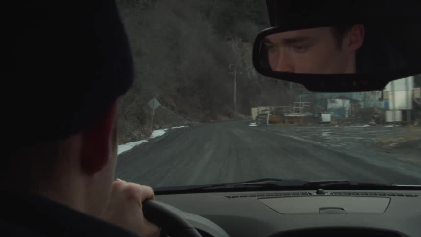 Man driving down road between cliffs and a body of water