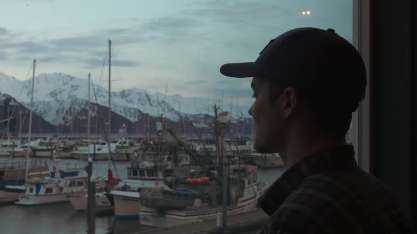 A man wearing a cap looks at the boats stationed in the lake