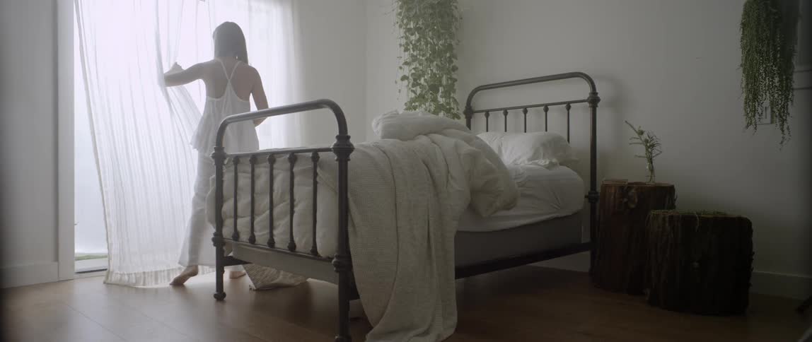 A woman gets out of bed and walks to the window