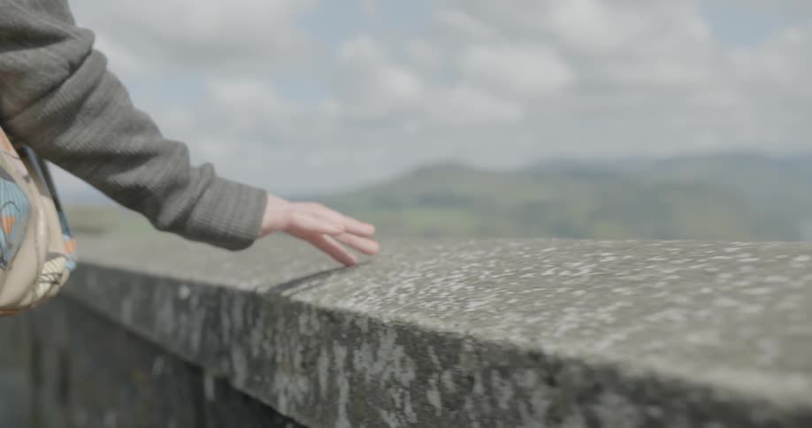 A white woman walks while touching her fingers to a stone bridge