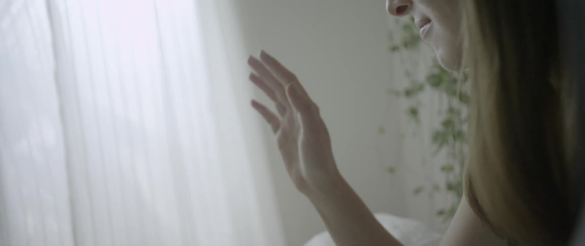 A woman sits in bed staring at her hand