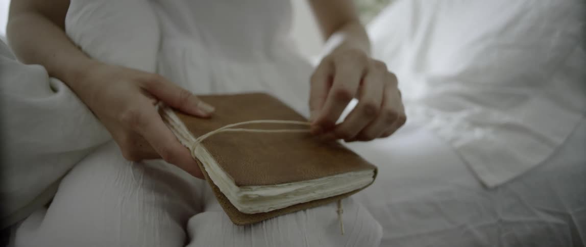 A woman is looking at her diary sitting on the edge of the bed